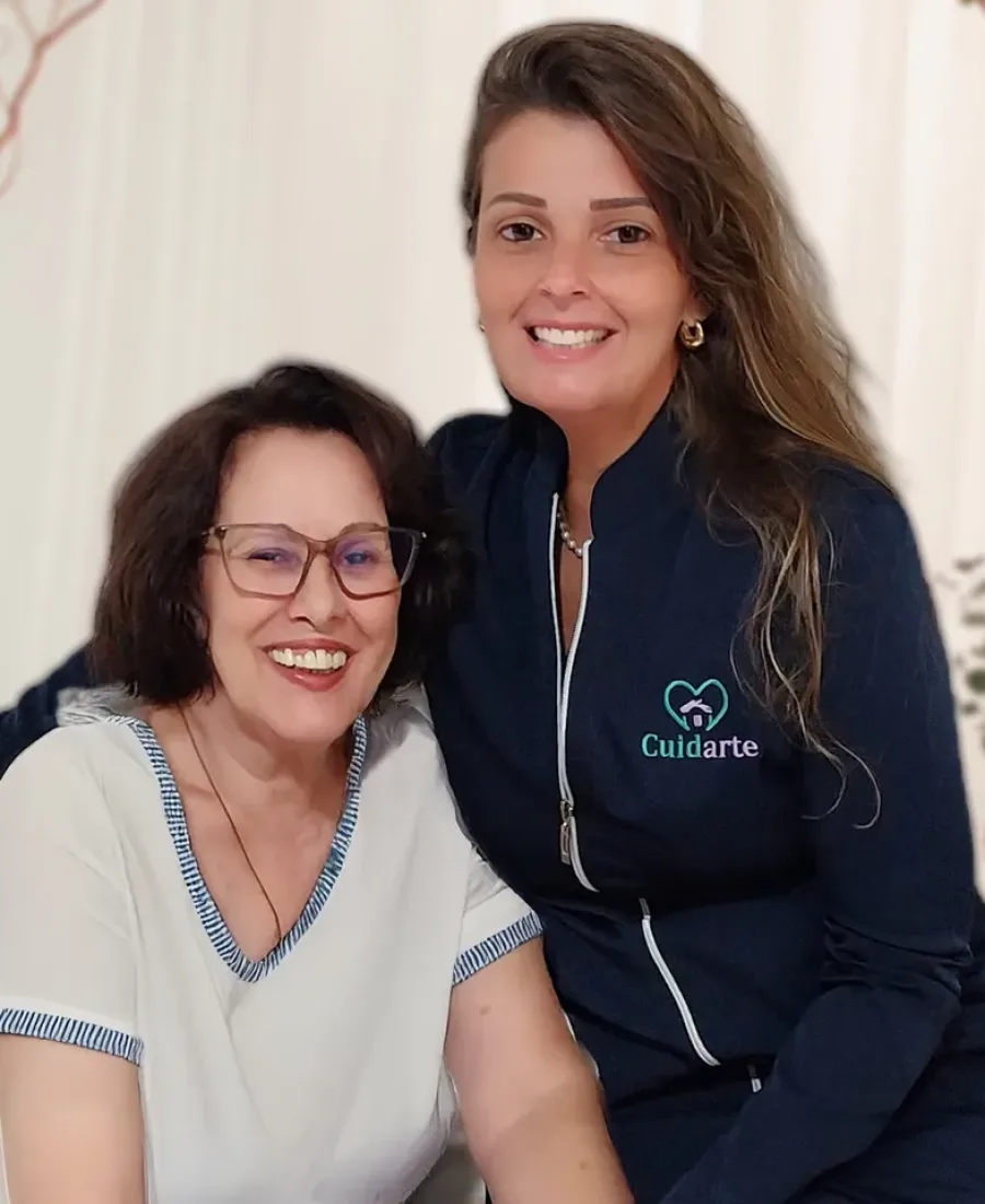 Cuidadora e cliente sorrindo lado a lado dentro de casa